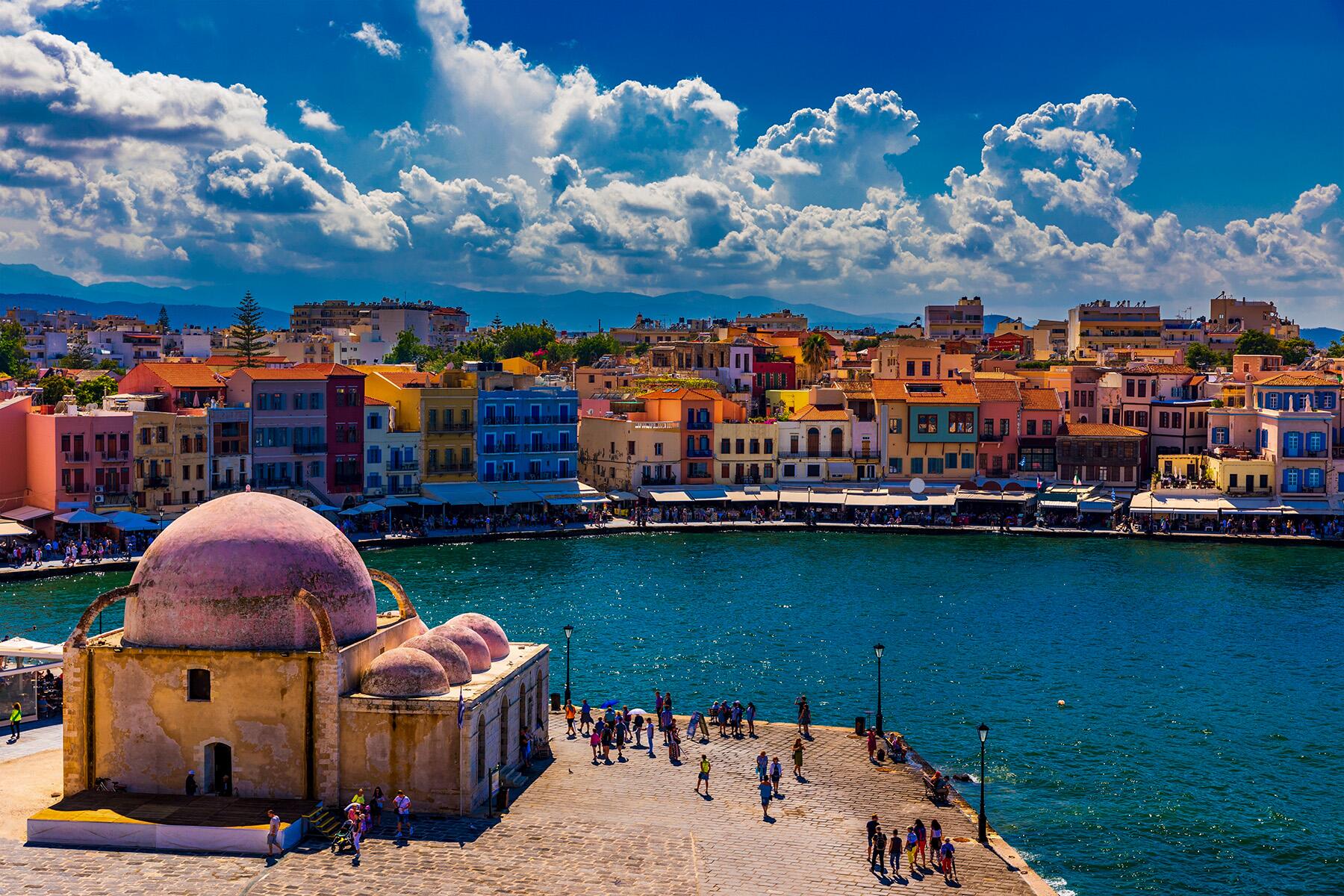 Colorful waterfront buildings and a domed structure by the sea under a cloudy sky.