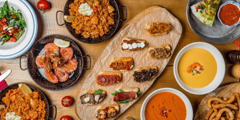 Assorted Spanish tapas and soups arranged on a wooden table.