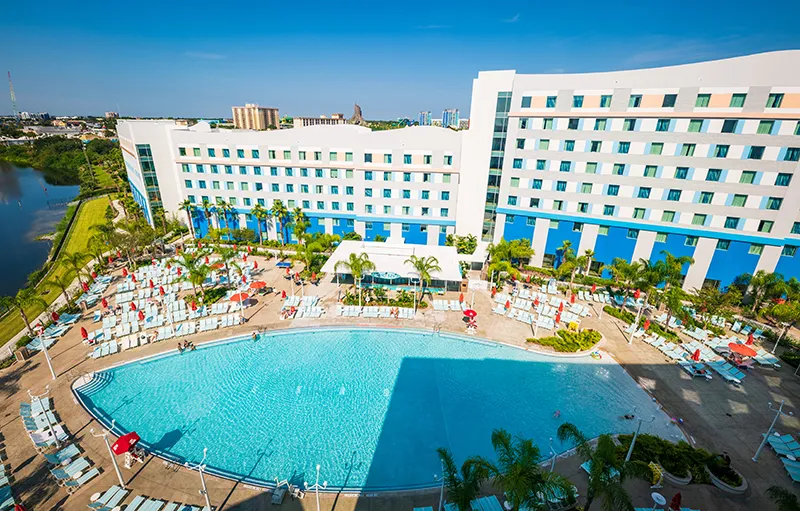 Large hotel with a curved swimming pool and surrounding palm trees.