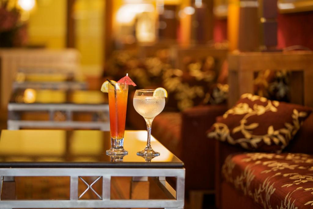 Two cocktails with fruit garnishes sit on a table in a softly lit lounge.