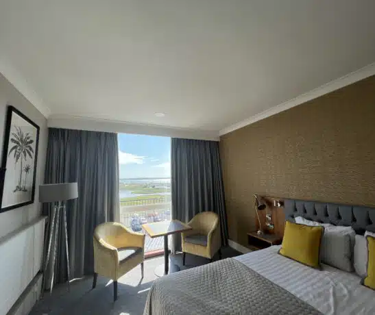 Hotel room with a bed, chairs, table, and window view of a landscape.