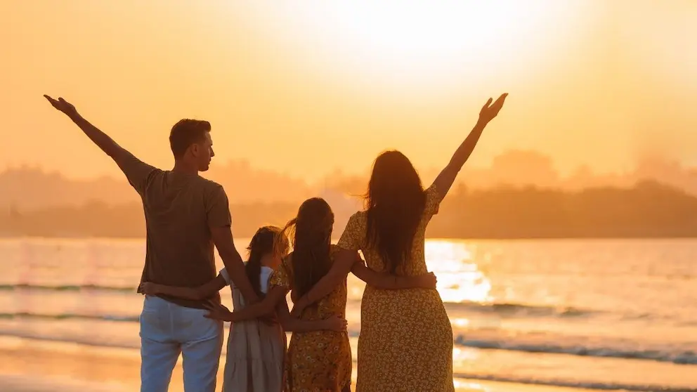 Family of four embracing, watching sunset on the beach.