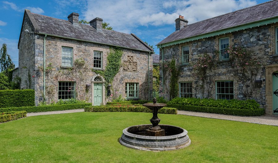 Two large stone houses with a manicured lawn and a stone fountain in the center.
