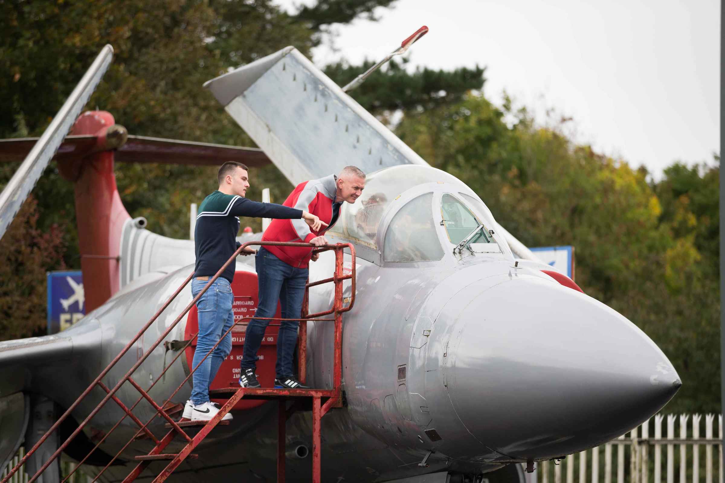 Two people examining a vintage aircraft cockpit on a metal staircase.