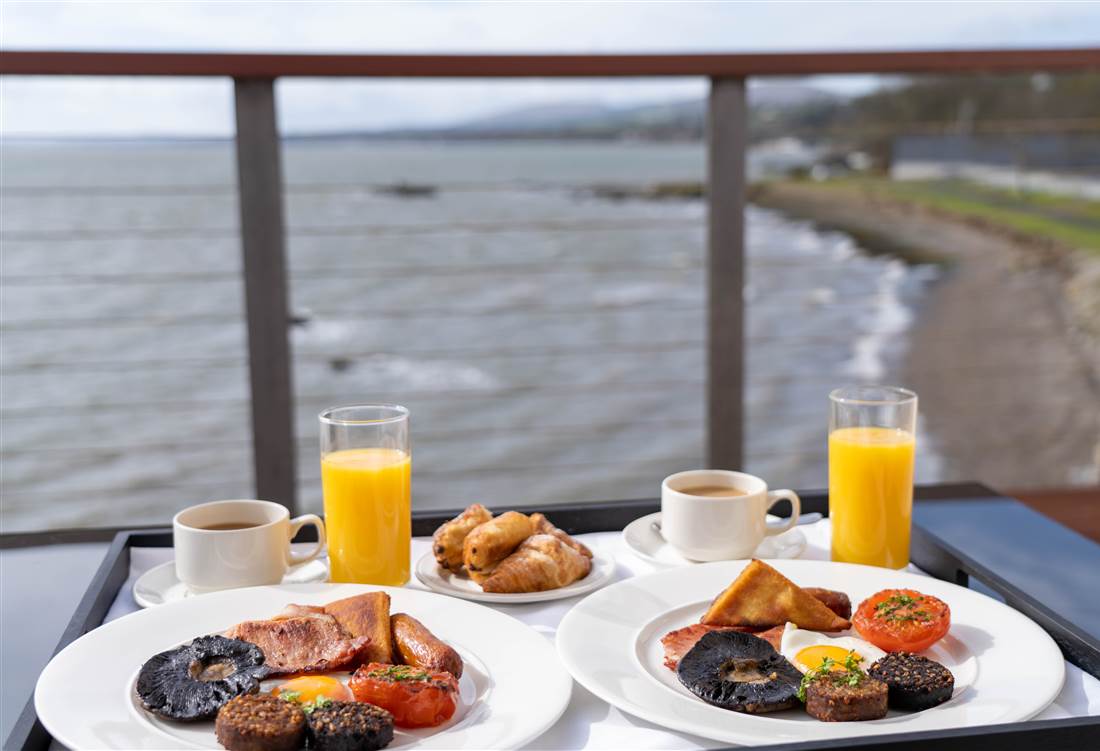 Two breakfast plates with drinks on a seaside deck.