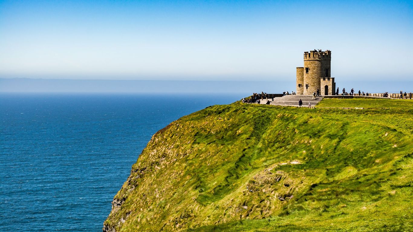 Stone tower on a grassy cliff overlooking the ocean under a clear blue sky.