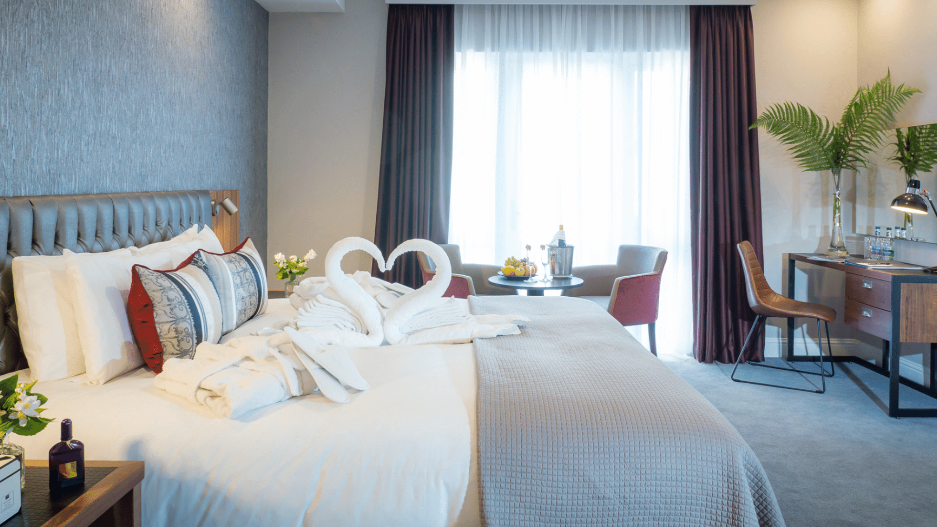 A modern hotel room with two swans made from towels sitting on the bed, forming a heart shape.
