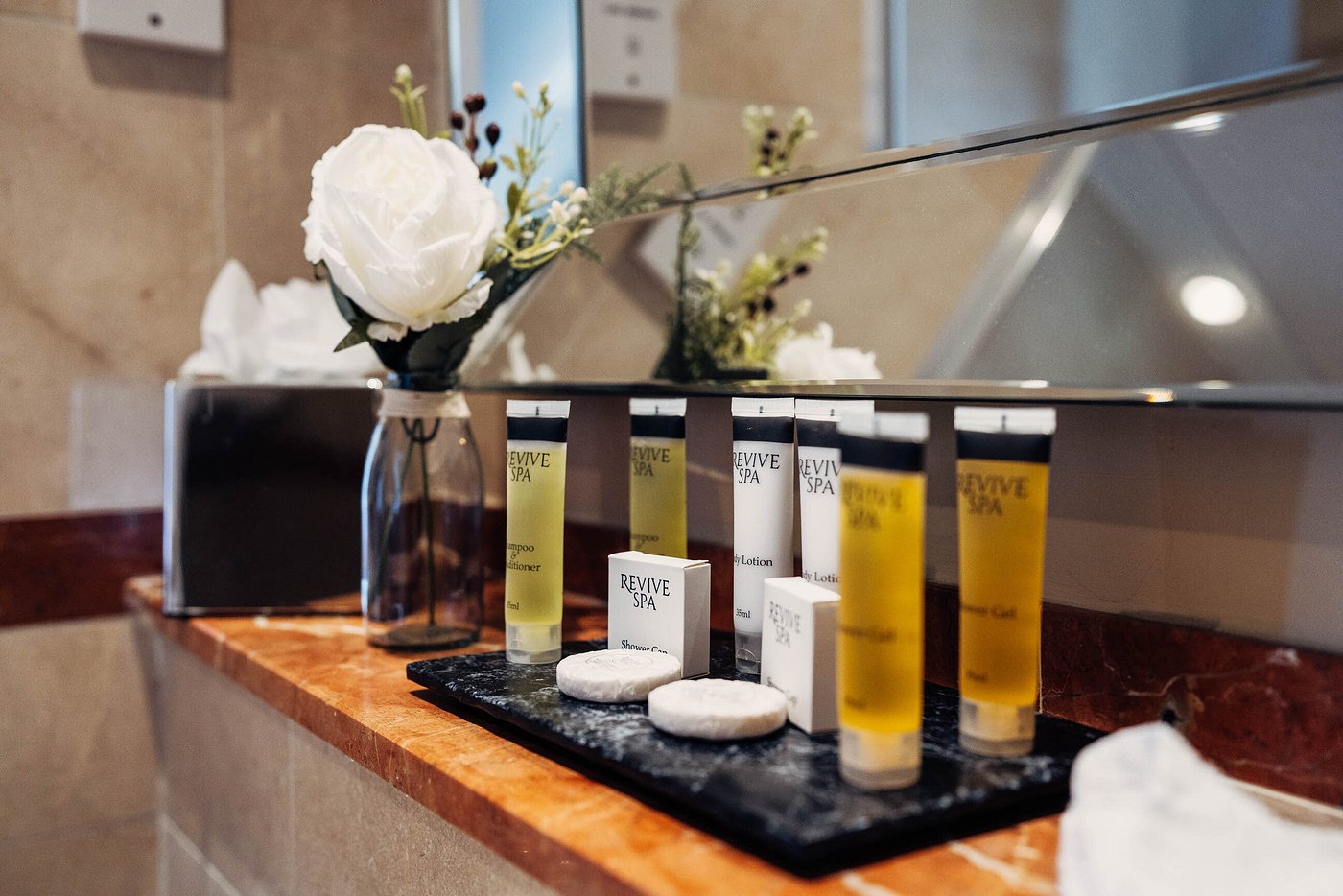 Bathroom counter with spa toiletries and a white rose in a vase.