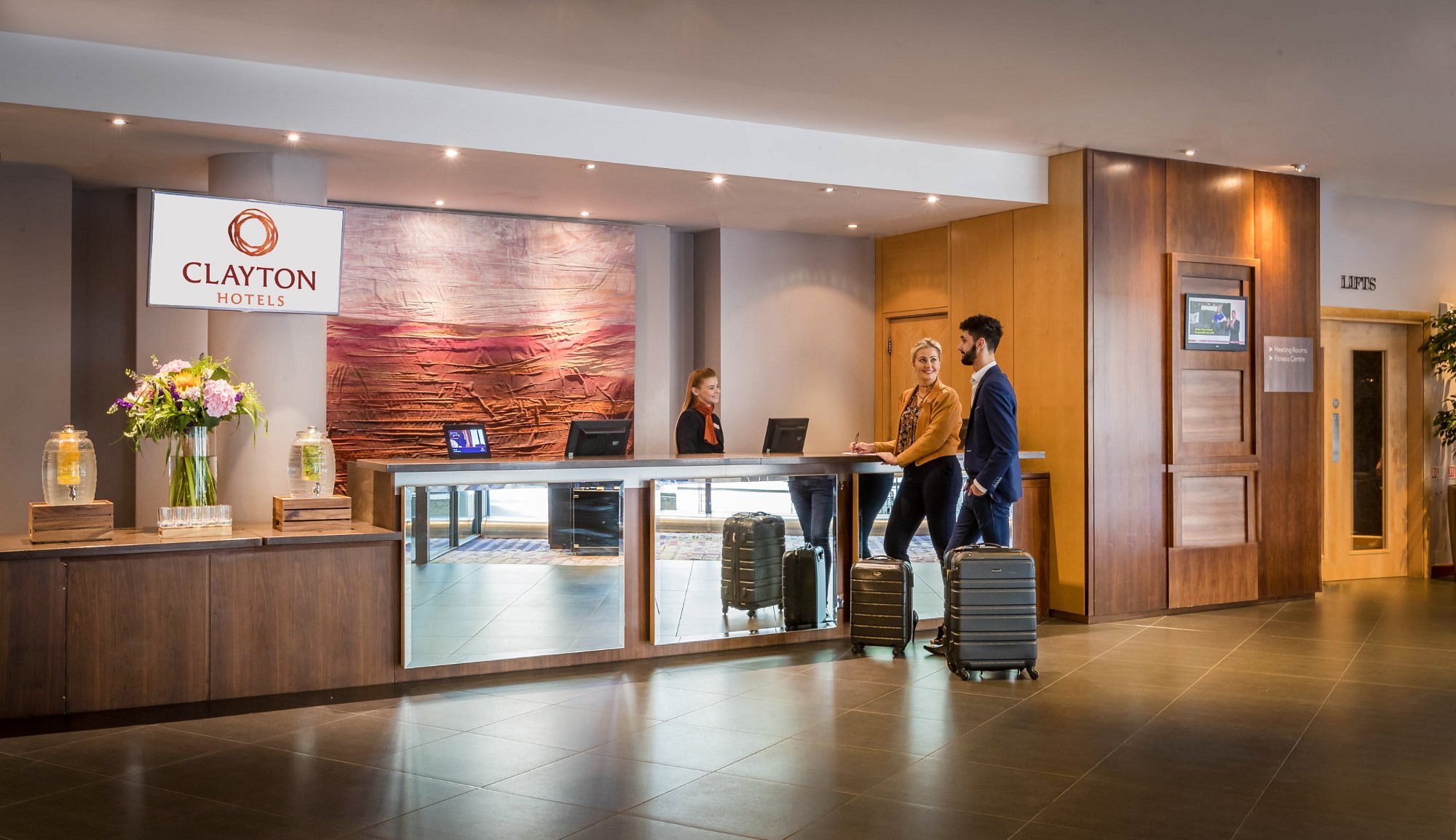 Hotel reception area with two guests and a receptionist.