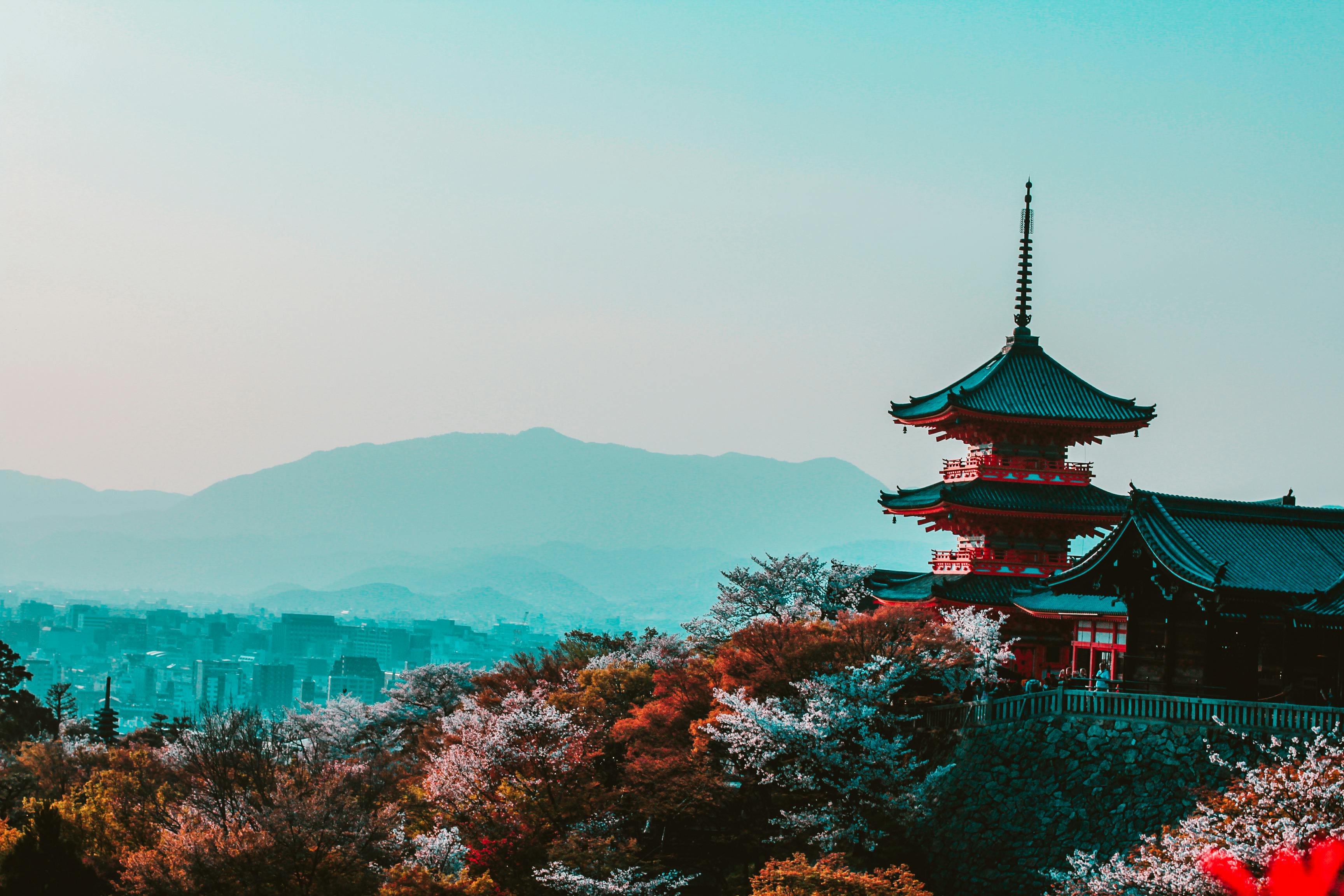 Traditional Japanese pagoda with cherry blossoms and mountains in the background.