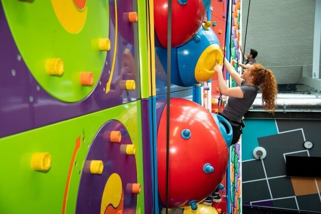 Person climbing a colorful indoor climbing wall with large round holds.