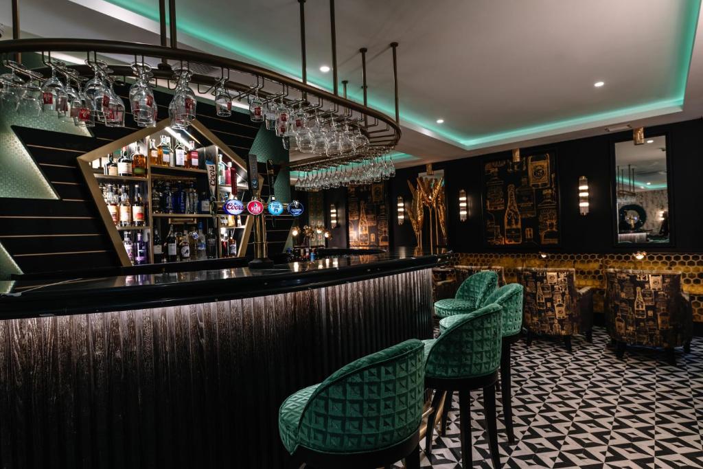 The interior of a stylish, dimly lit bar with green velvet stools and geometric black and white flooring.