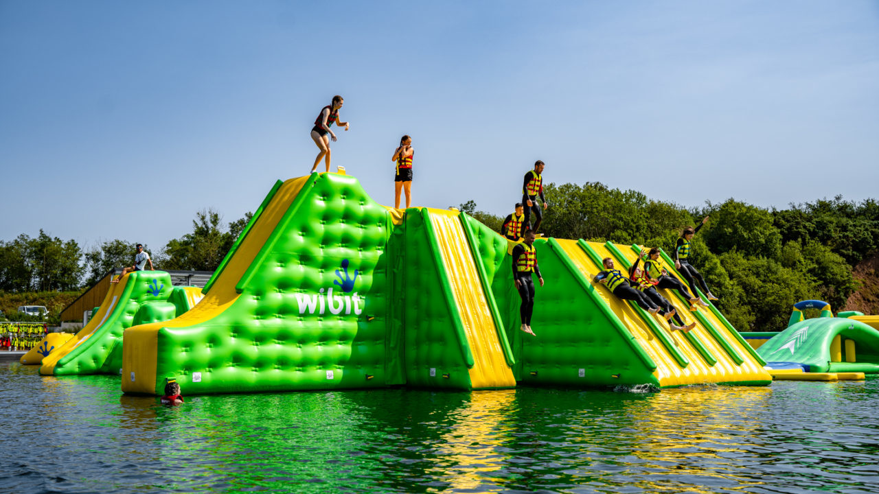 People enjoying a large inflatable water obstacle course on a sunny day.