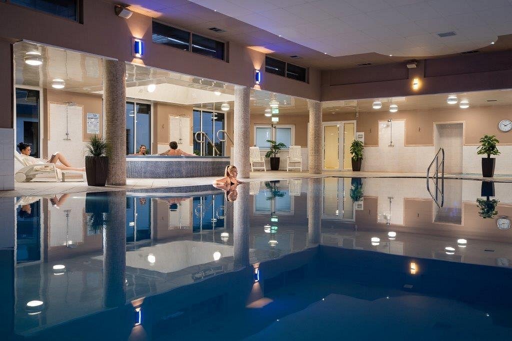 Indoor pool area with people relaxing in a hot tub and on lounge chairs.