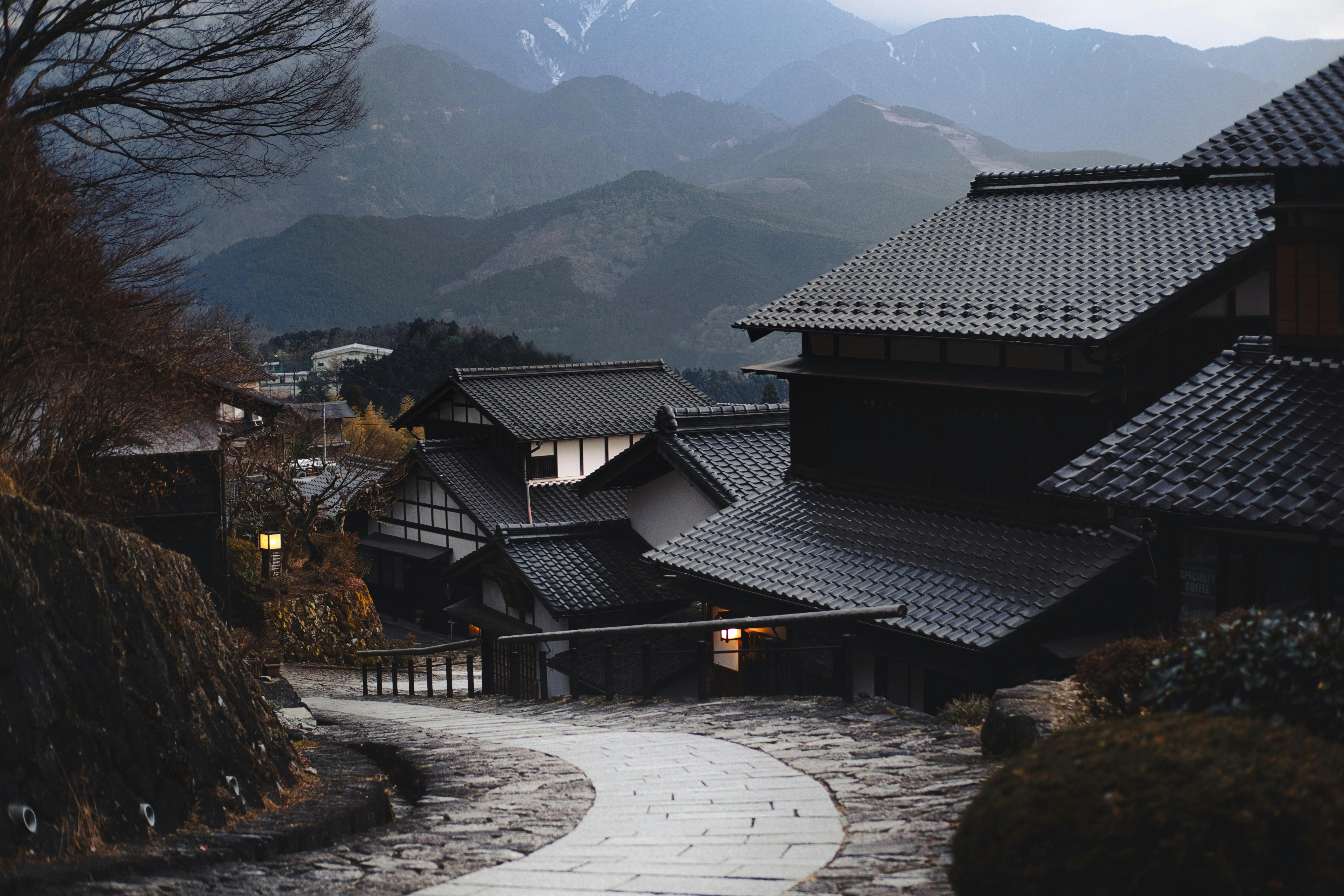 Traditional Japanese village with tiled roofs and mountain backdrop at dusk.