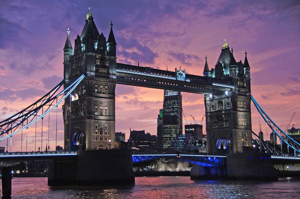 Illuminated bridge at sunset with city skyline in the background.