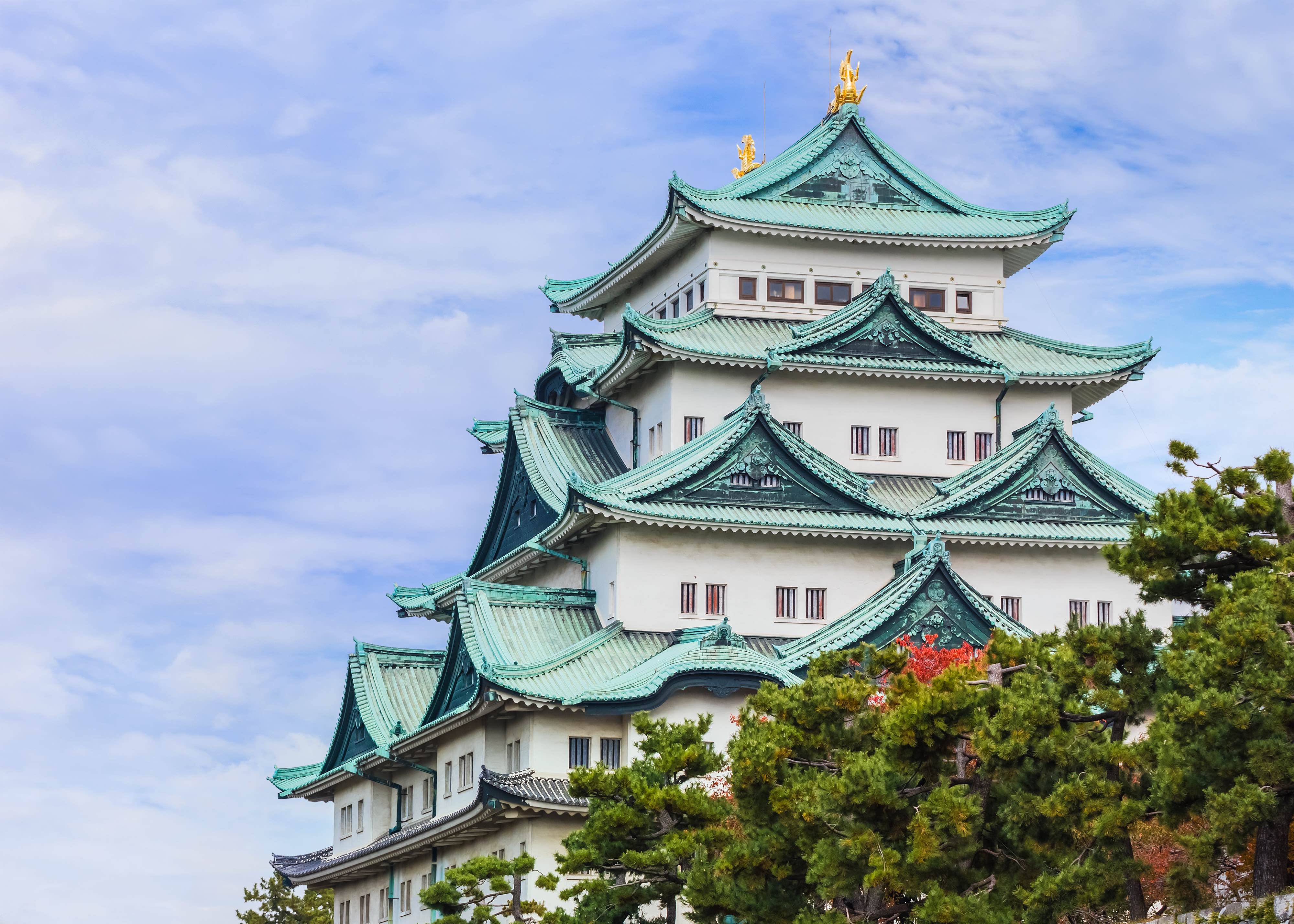 Traditional Japanese castle with green roofs and ornate details against a blue sky.