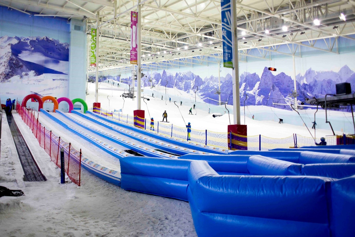 Indoor ski slope with snow, skiers, and colorful inflatable barriers.