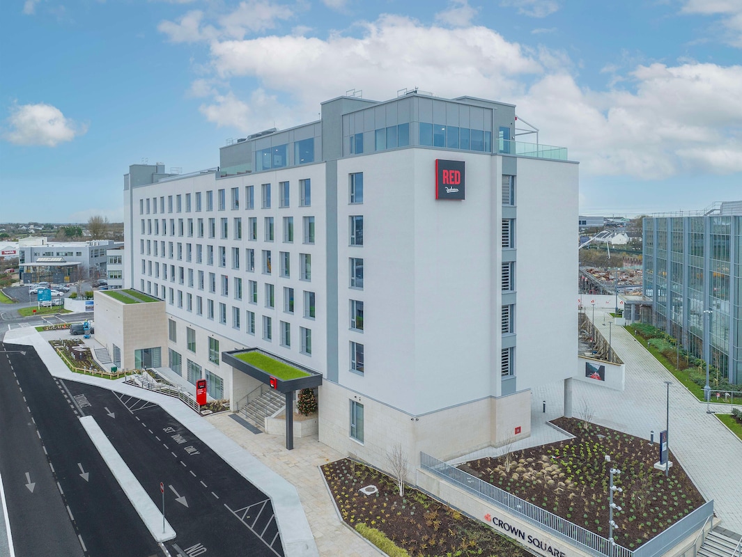 Modern multi-story hotel building with a sign reading 'RED' and landscaped surroundings.
