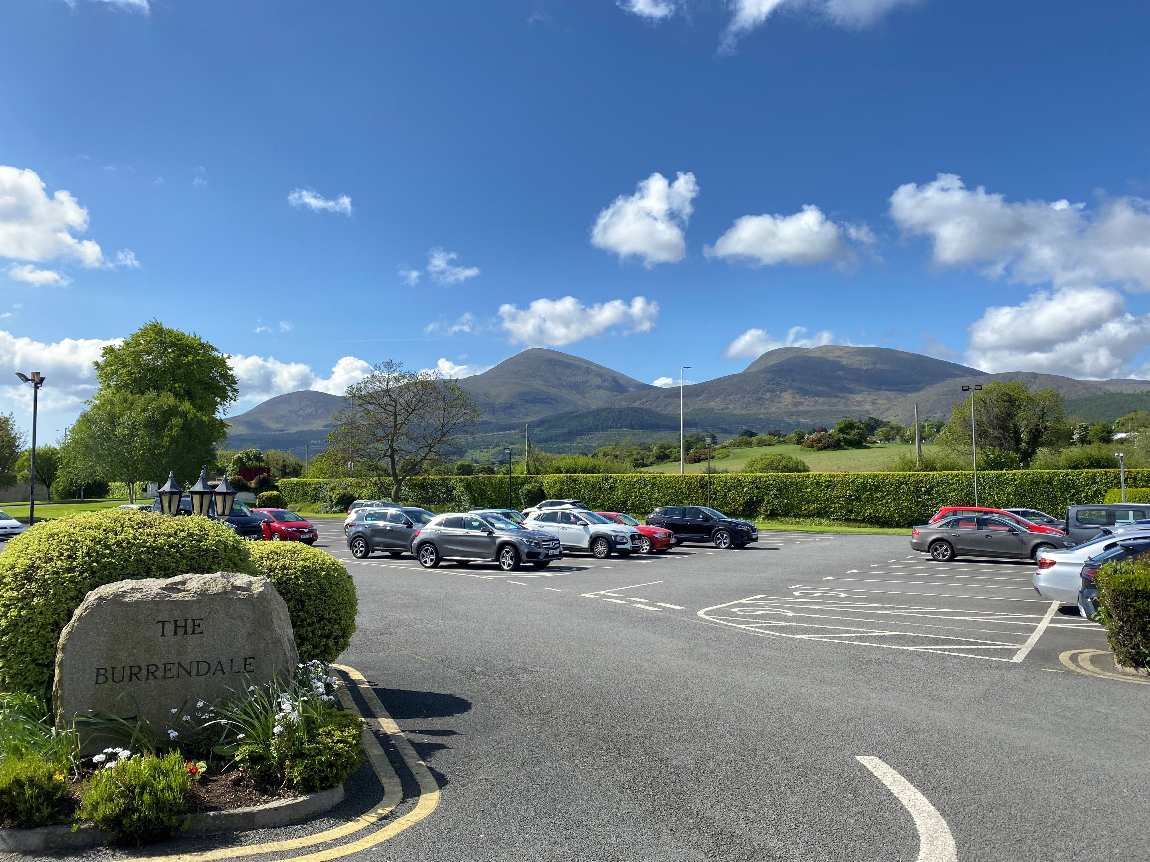 The Burrendale hotel parking lot, with cars parked against a backdrop of mountains on a sunny day.
