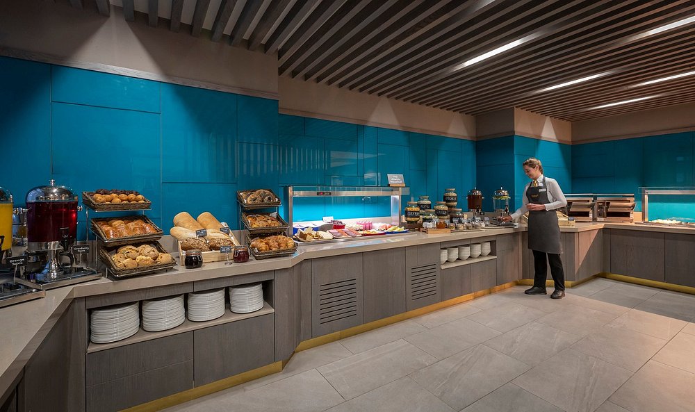 Buffet with pastries, bread, and a person serving food in a modern setting.