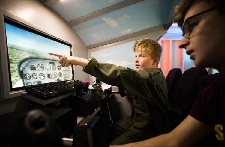 Two boys in a flight simulator, one pointing at the screen.