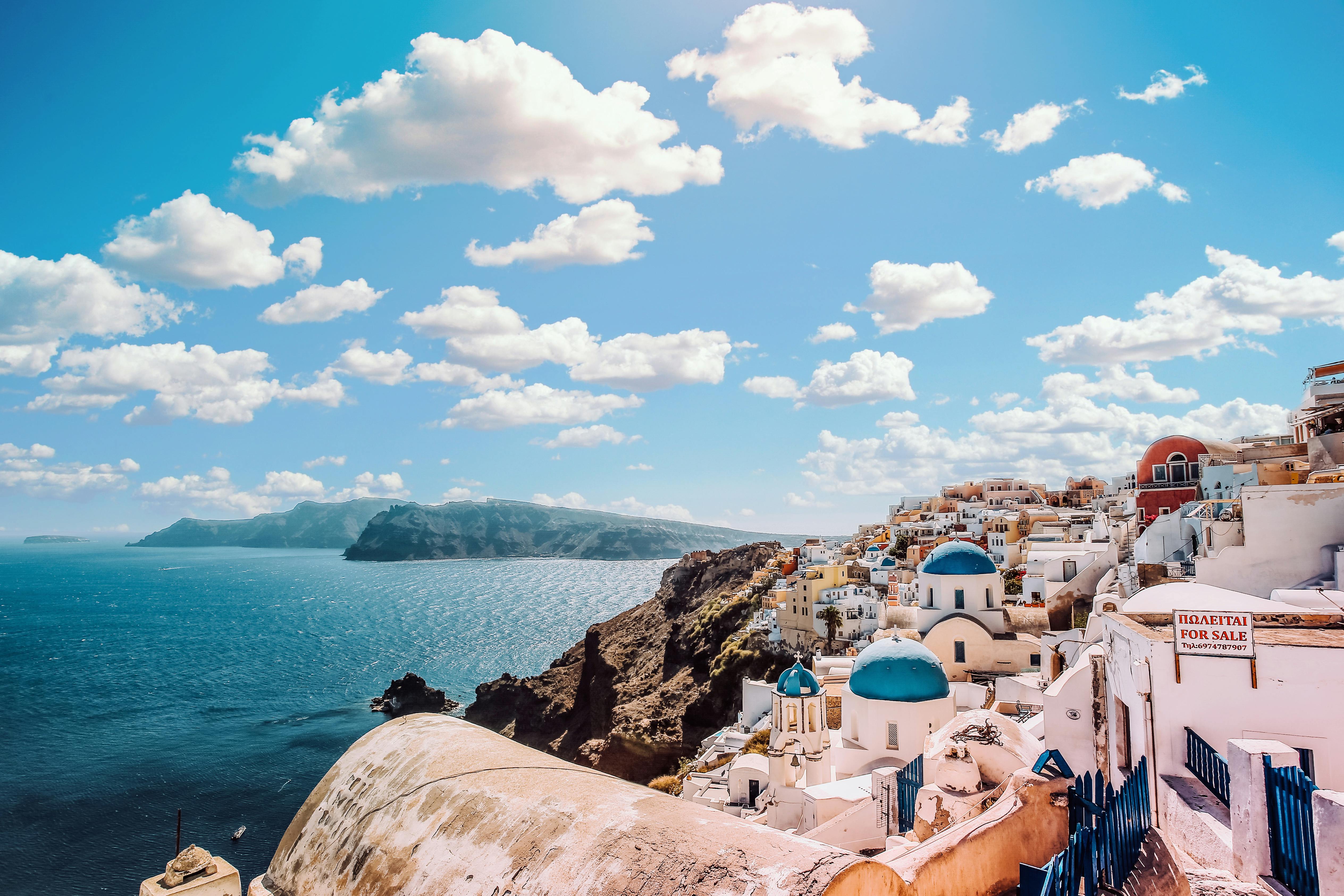 Scenic view of white buildings with blue domes by the sea under a cloudy sky.