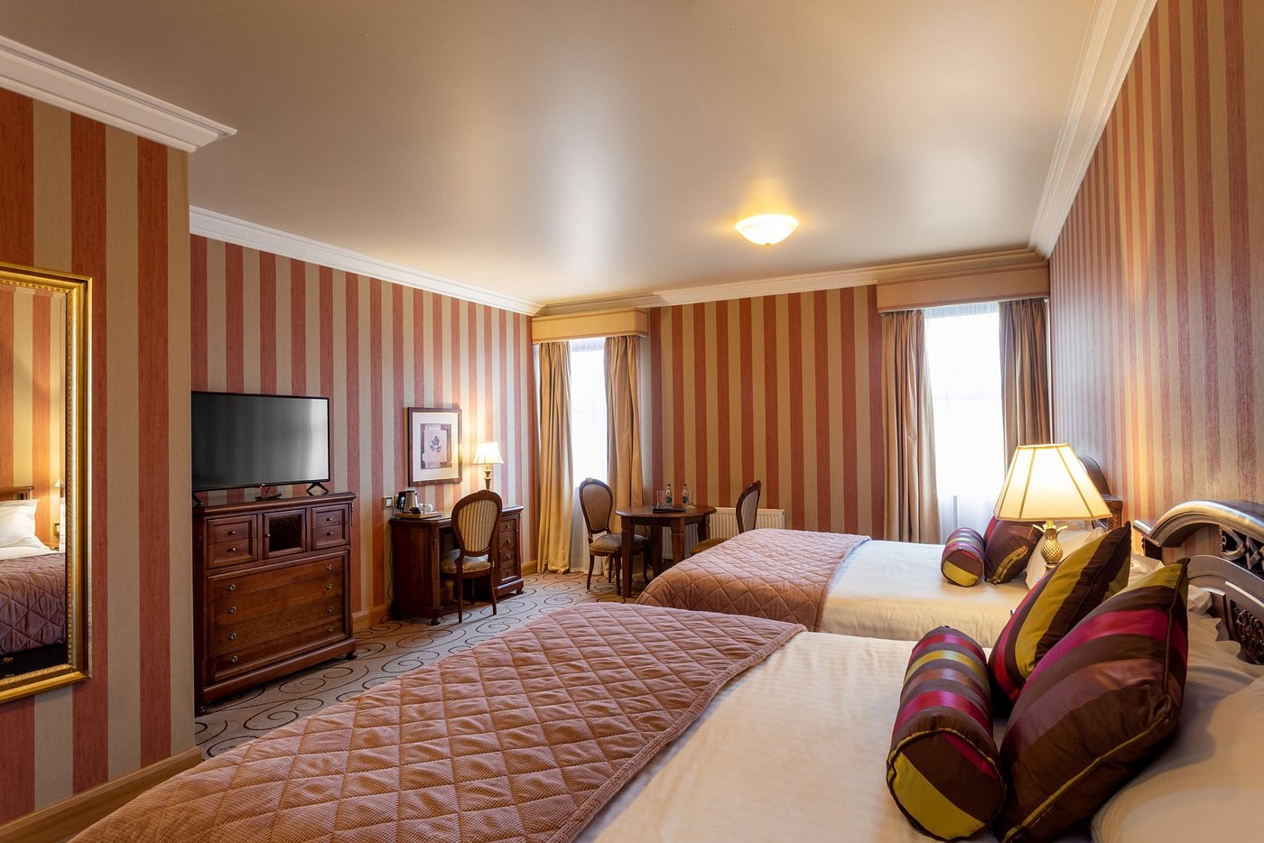 Hotel room with two beds, striped walls, and a TV on a wooden dresser.
