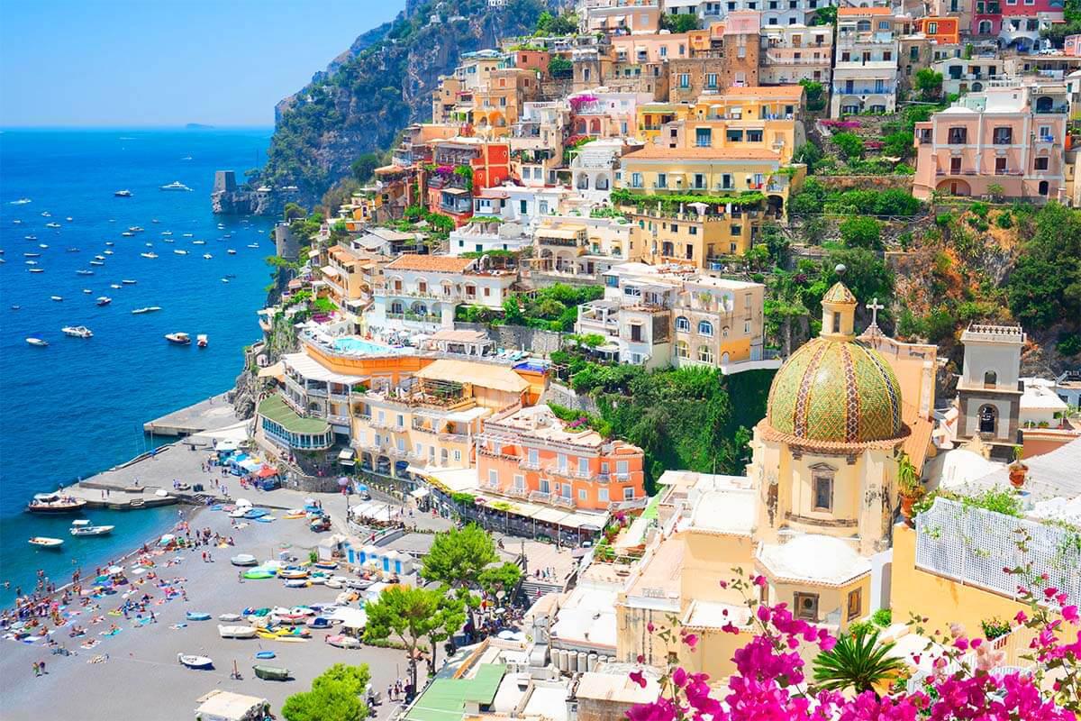 Colorful hillside town with beach, boats, and vibrant flowers.