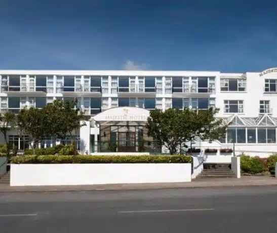 A white multi-story hotel building with trees and a clear blue sky.