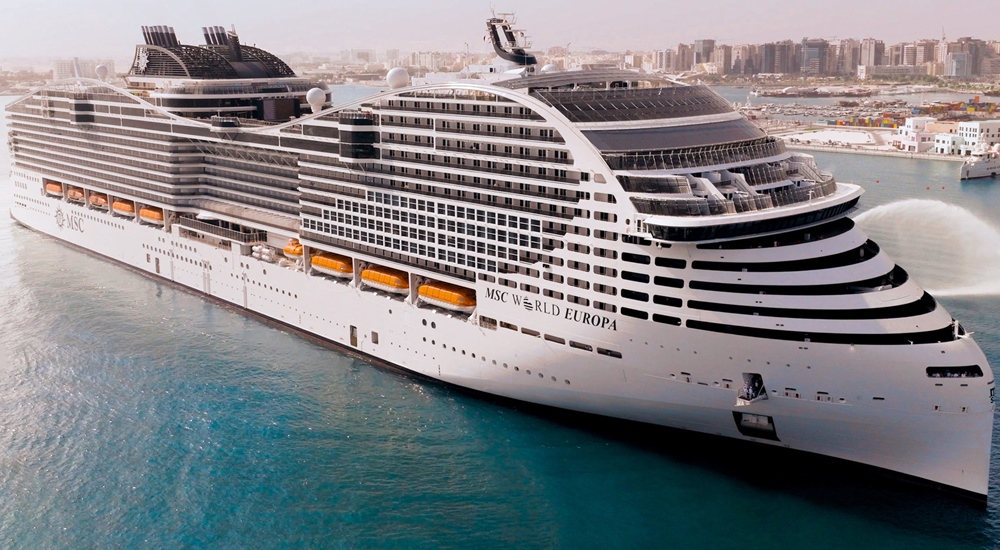 Large cruise ship docked in a harbor with city skyline in the background.