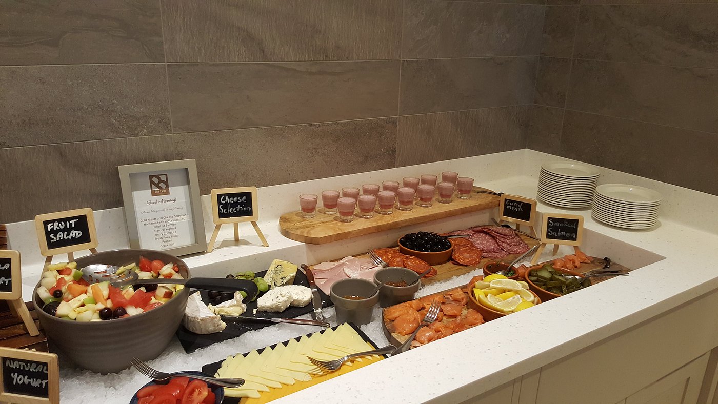 Buffet with fruit salad, cheese, cold meats, smoked salmon, and small glasses of pink drink.