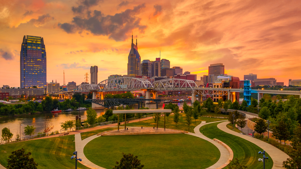 The Nashville skyline viewed from a park across the river during a vibrant orange sunset.
