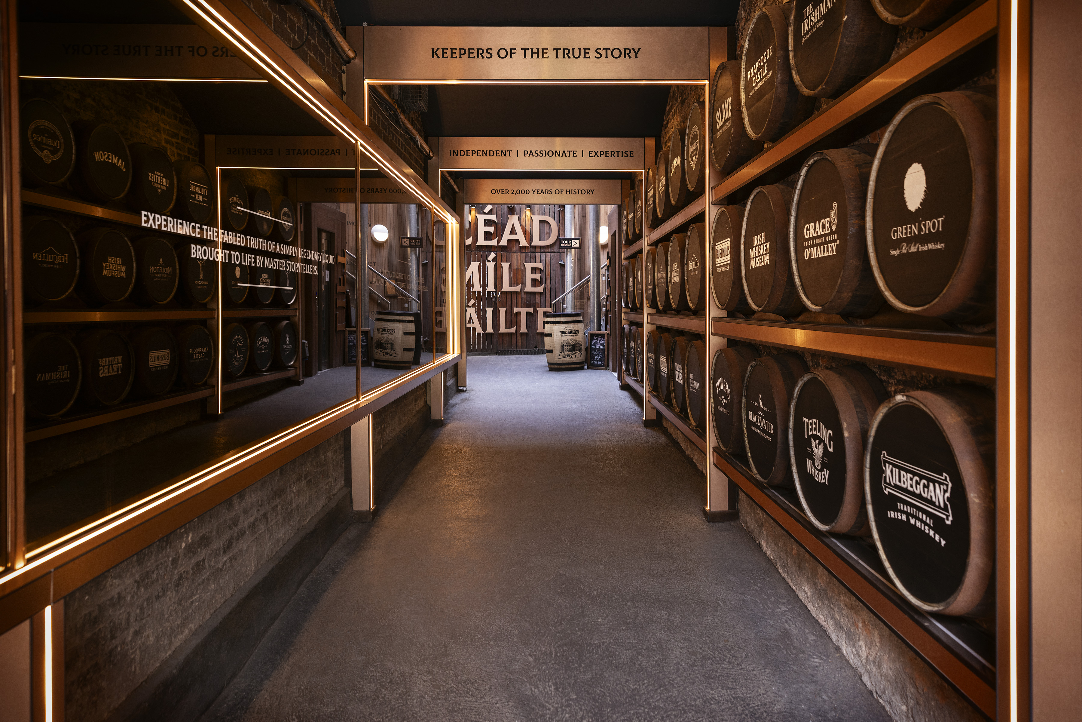 Corridor lined with whiskey barrels and illuminated signs.