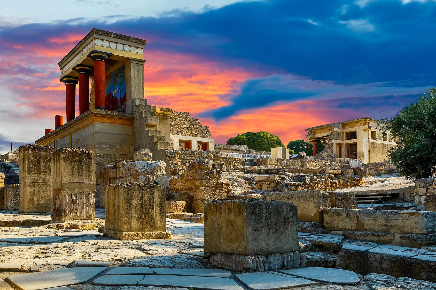 Ancient ruins with red columns under a vibrant sunset sky.