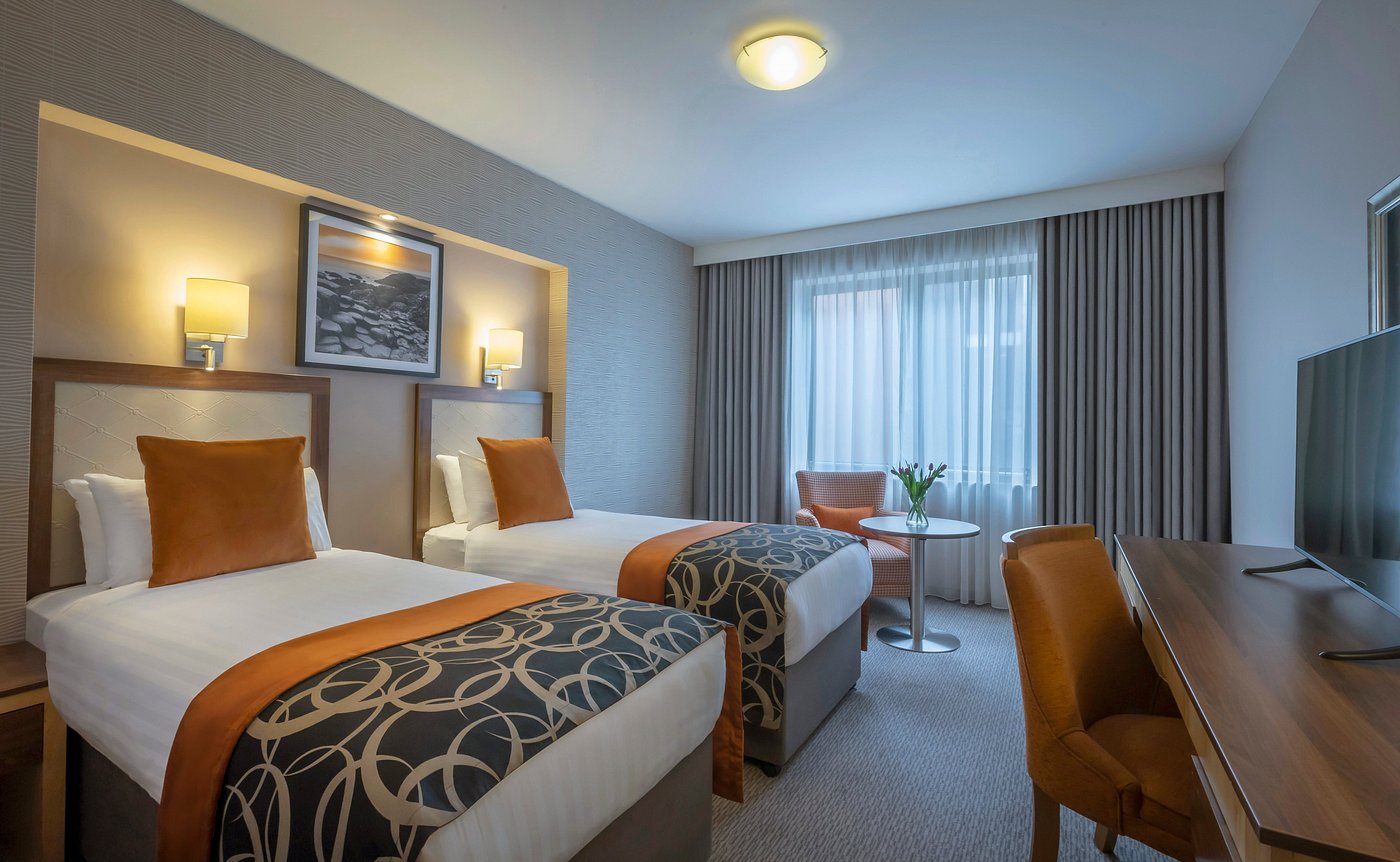 Hotel room with two beds, orange accents, and a window with curtains.