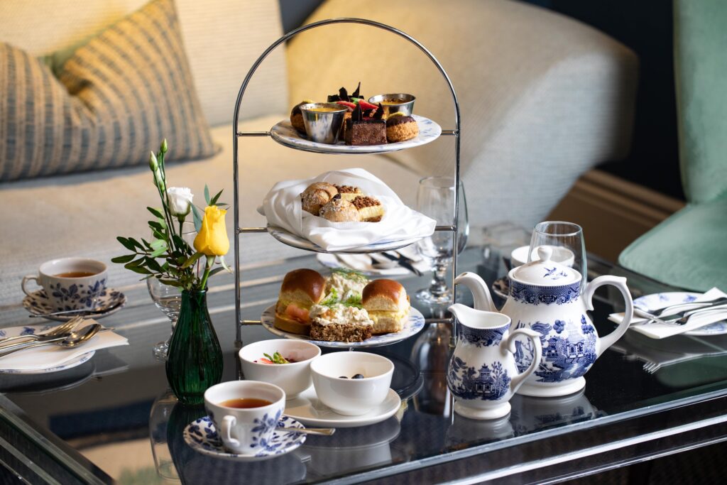 An afternoon tea service with a three-tiered stand of food, teacups, and a teapot on a table.
