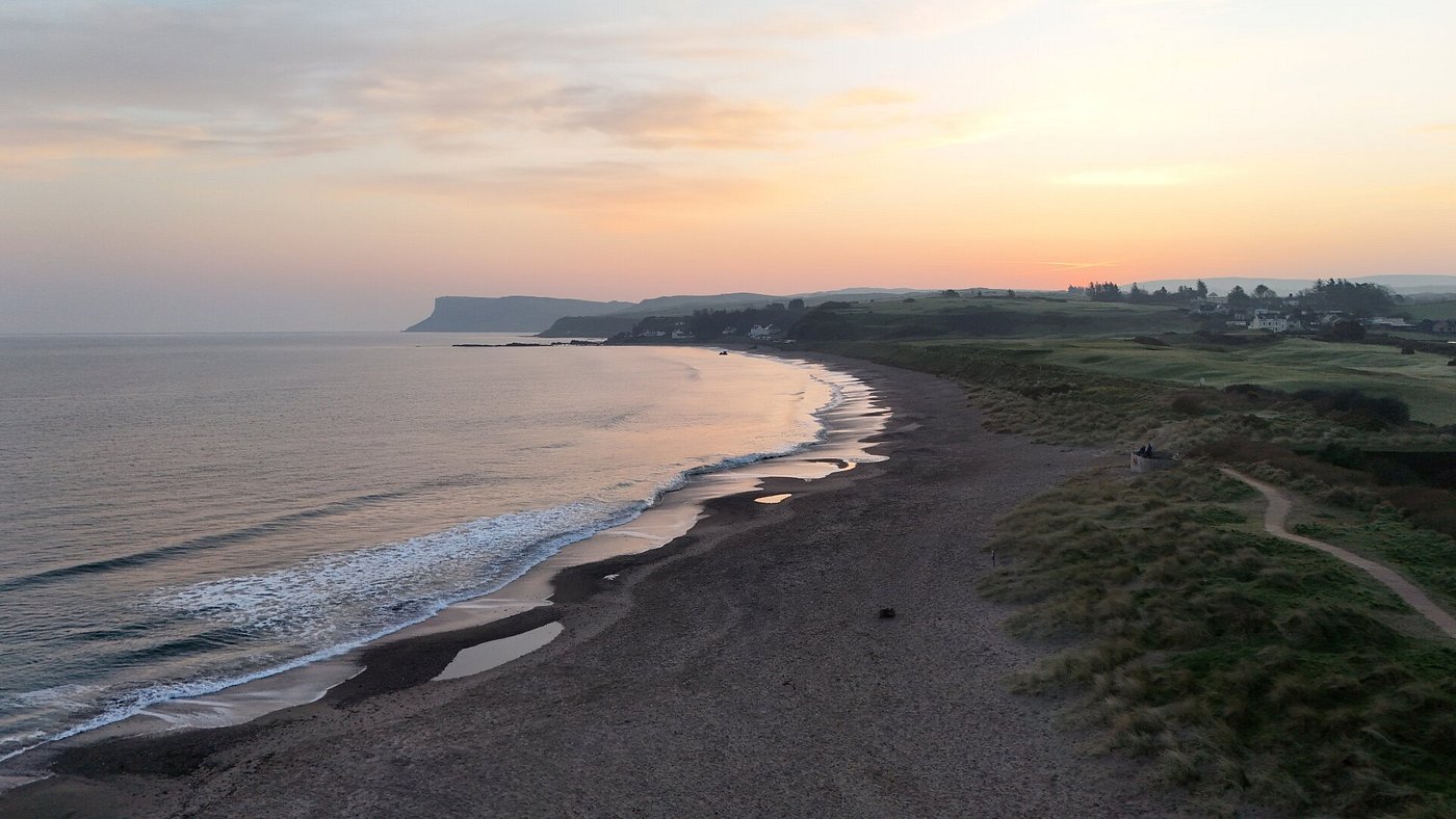A serene beach at sunset with gentle waves and distant hills.