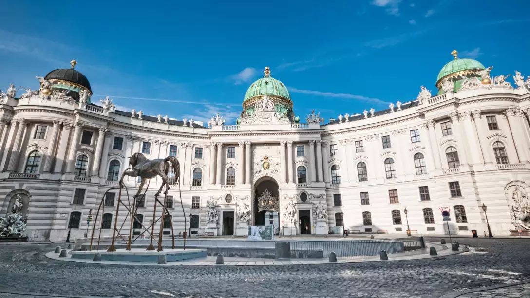 The Hofburg Palace in Vienna with a modern horse sculpture in the cobblestone plaza.