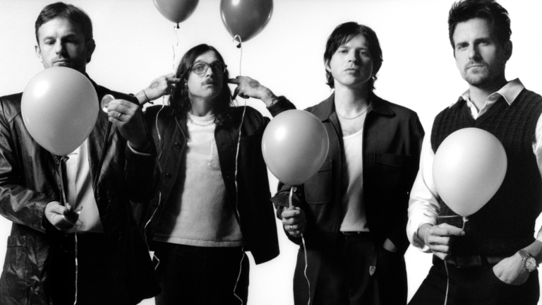 A black and white photograph of four men standing side-by-side, each holding a balloon.