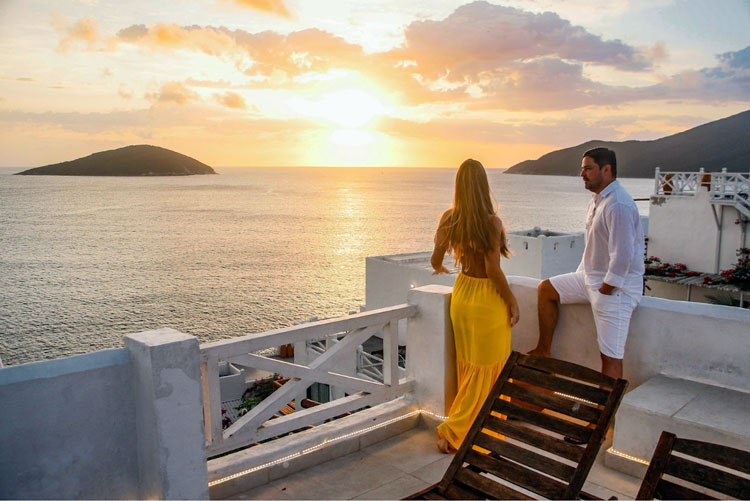 A couple on a balcony watching a sunset over the ocean.