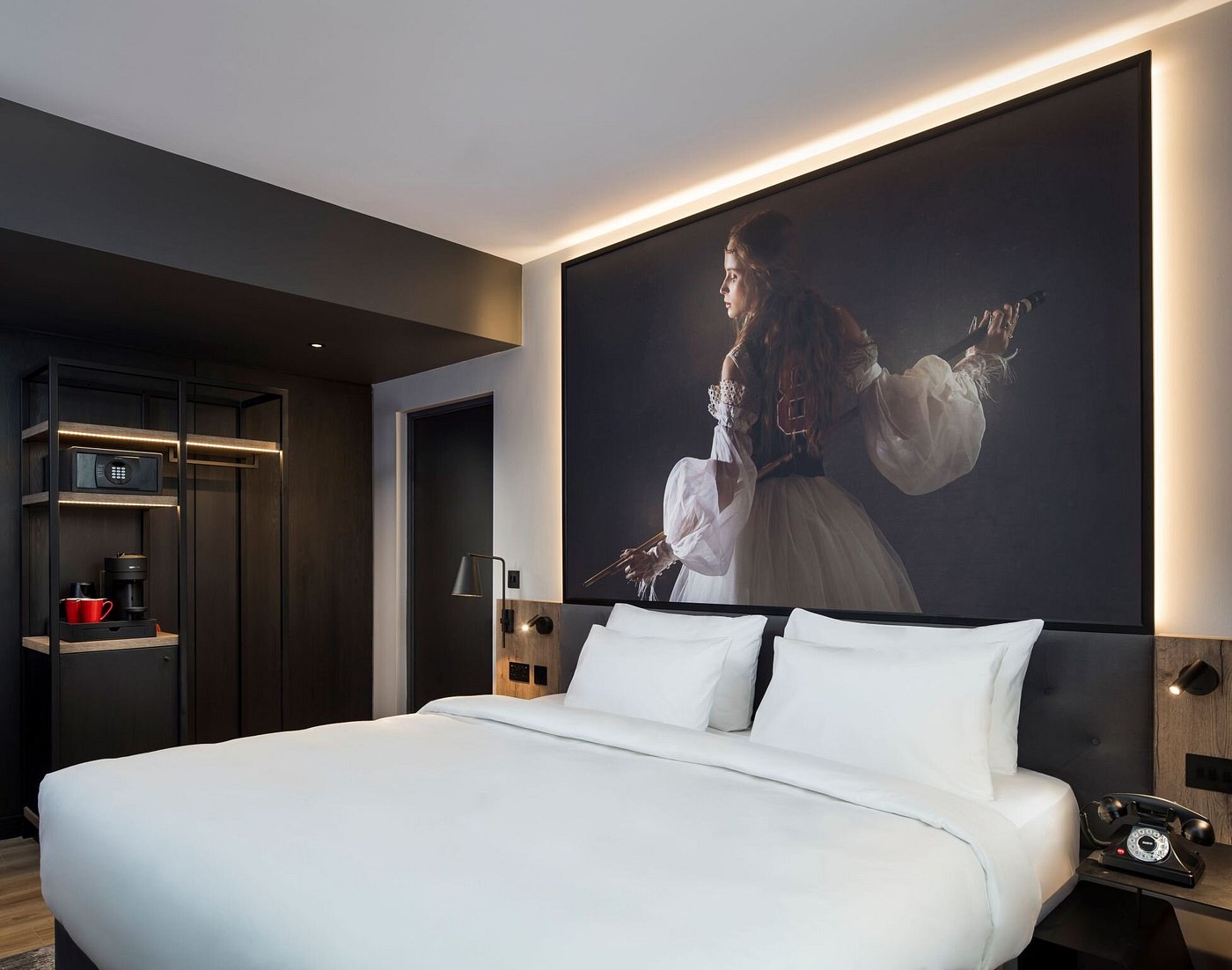 Modern hotel room with large painting above bed, coffee maker, and vintage phone.