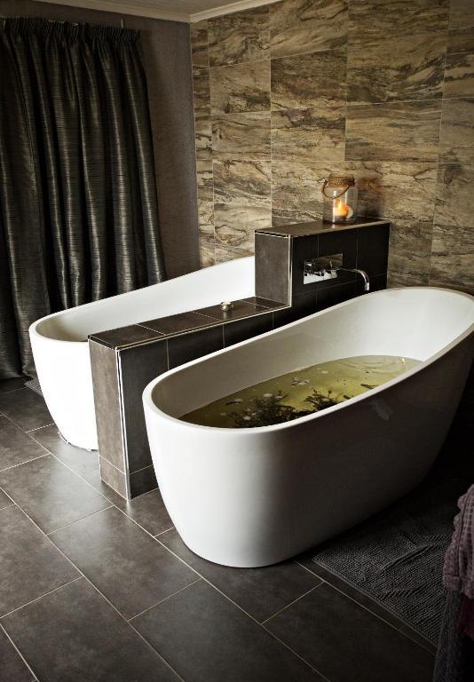 Two white freestanding bathtubs in a modern bathroom with tiled walls and floor.