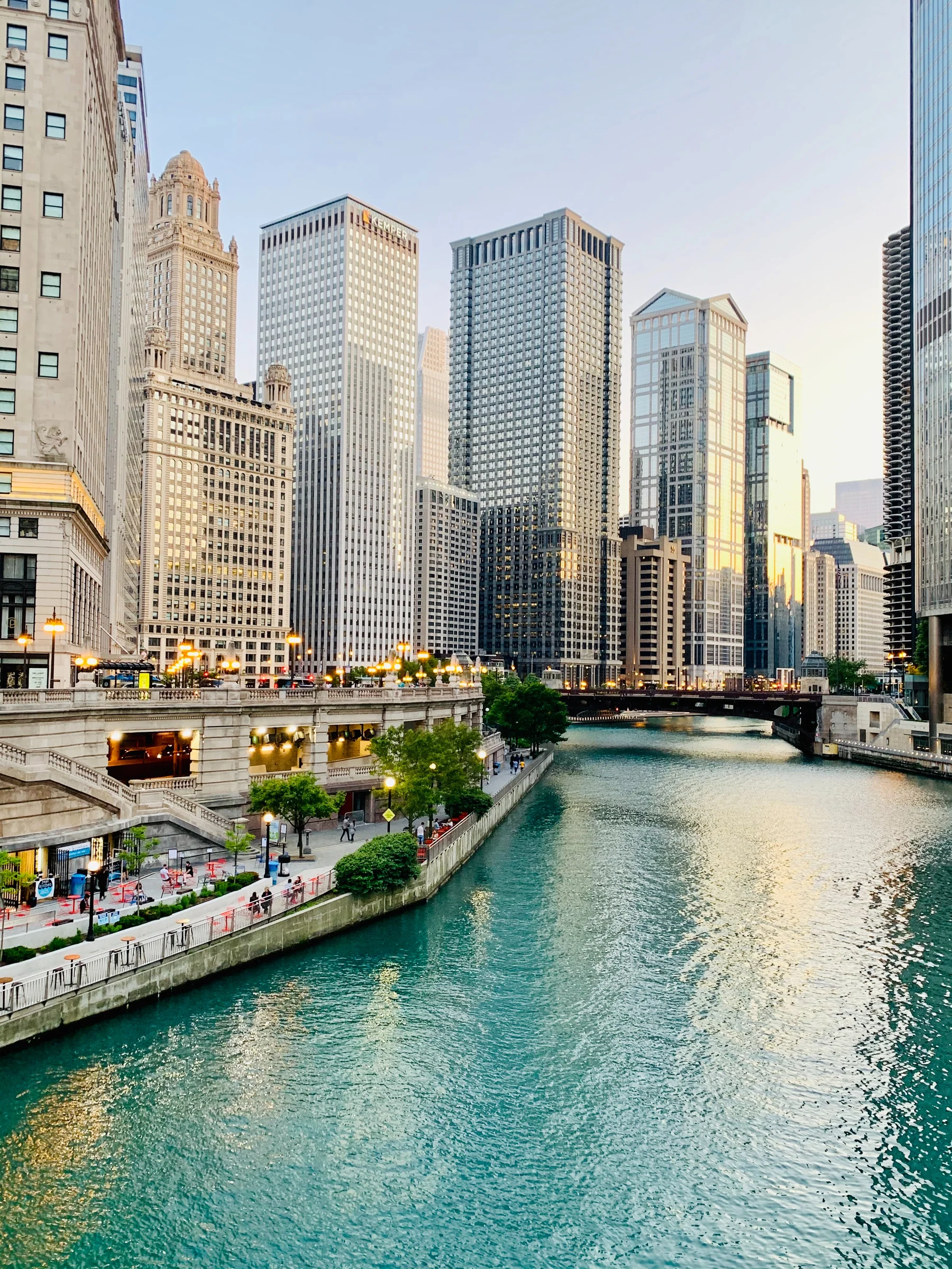 Cityscape with tall buildings and a river reflecting the evening light.