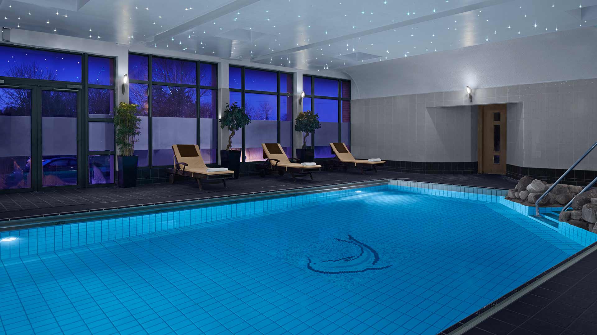 An indoor swimming pool at night with lounge chairs and a ceiling lit with tiny, star-like lights.