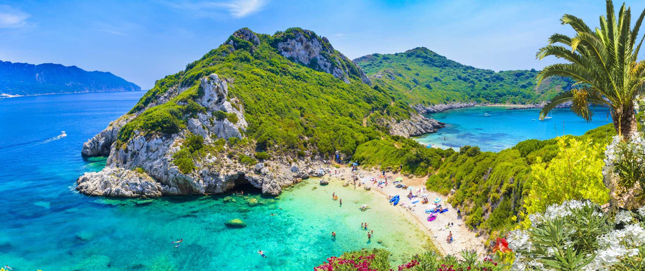 A scenic view of a beach cove with turquoise water, green hills, and people enjoying a sunny day.