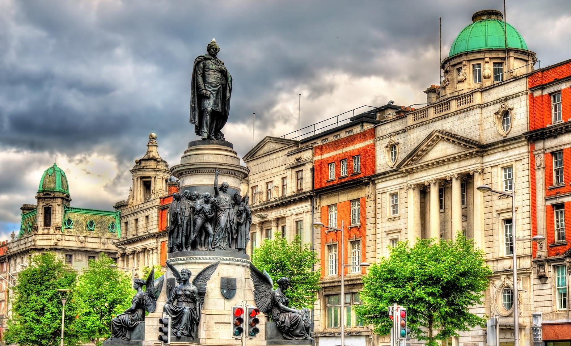 Statue on a pedestal with surrounding historic buildings and cloudy sky.