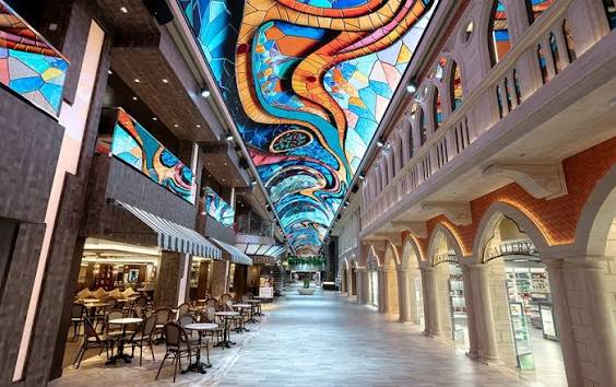 A long indoor promenade with a colorful, artistic LED screen ceiling and shops on either side.