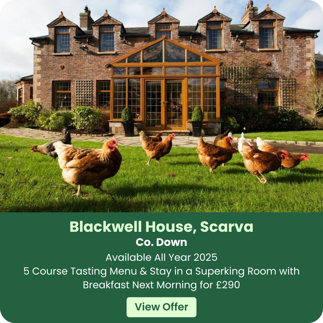 Chickens on grass in front of a brick house with large windows.