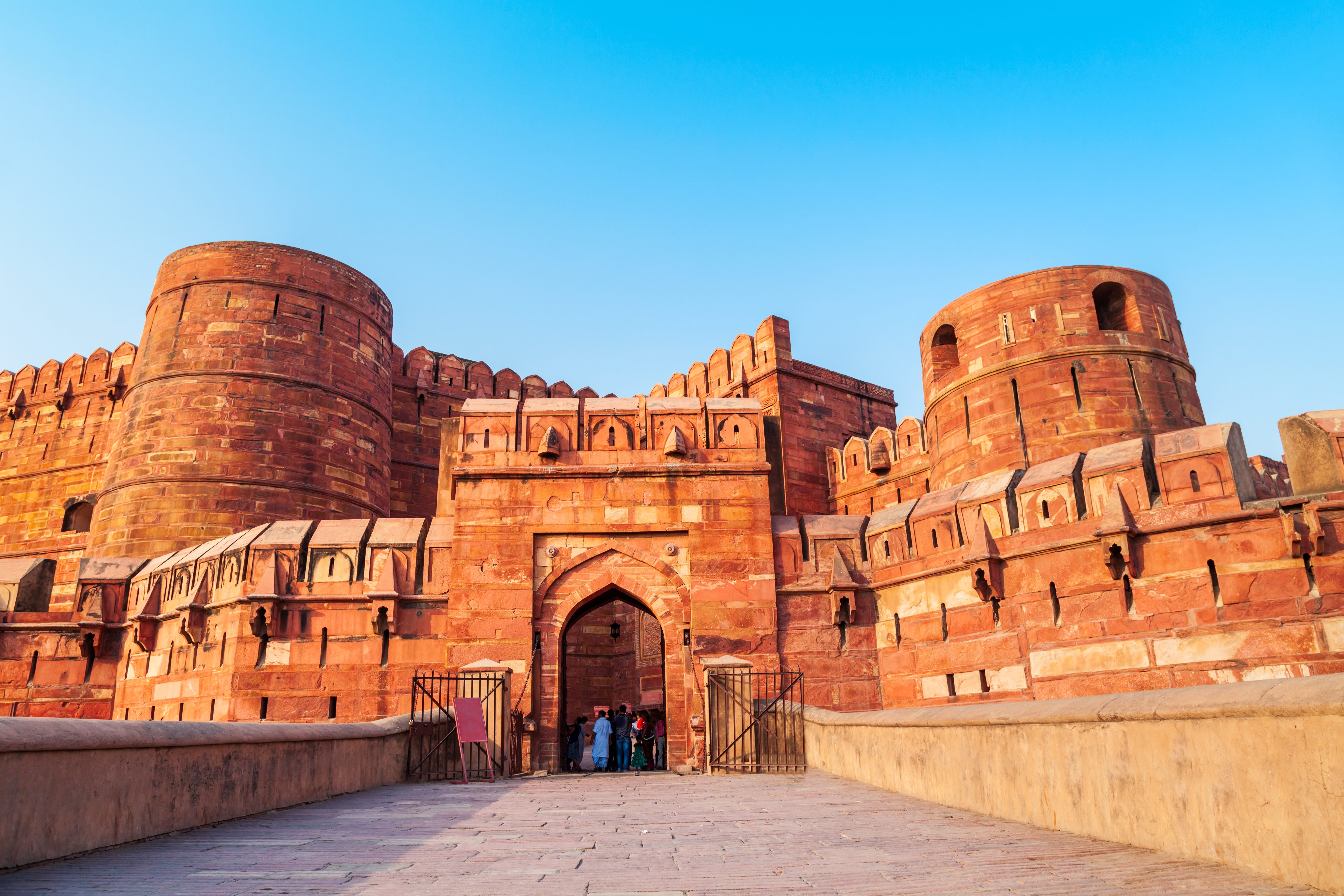 Red sandstone fort entrance with round towers and blue sky.